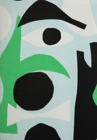 Abstract textileontwerp met zwarte, groene en witte vormen op een lichtblauwe achtergrond. De vormen omvatten cirkels, ogen en krommingen.