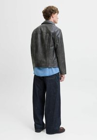 Chaqueta de cuero gris oscuro para hombre con un diseño de cuello, combinada con una camisa de mezclilla azul y jeans oscuros de corte holgado. Detalles de construcción simples.