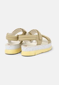 Beige Sandalen mit verstellbaren Riemen und einer gesprenkelten weißen Plattformsohle. Die Sohle hat einen gelben Akzent und ein strukturiertes Fußbett für zusätzlichen Komfort.