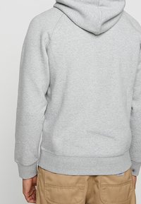 Szary hoodie z kapturem o miękkiej fakturze, z rękawami raglanowymi i kieszenią typu kangur, w połączeniu z jasnobrązowymi spodniami cargo.