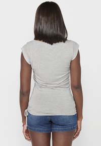 Top gris de manga corta con un diseño fruncido en la parte posterior, lazos en los laterales y un patrón floral en los hombros, combinado con pantalones cortos de mezclilla.