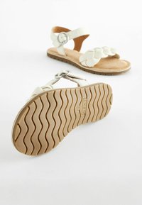 Vita sandaler med flätad design, justerbar rem med metalldekor och en texturerad beige sula. Slätt, mjukt material.