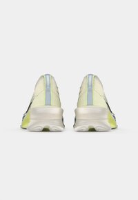 Πίσω όψη αθλητικών παπουτσιών σε ανοιχτό πράσινο χρώμα, με υφασμάτινη επάνω πλευρά με υφή, κίτρινες λεπτομέρειες και χοντρή, αφρώδη σχεδίαση σόλας.