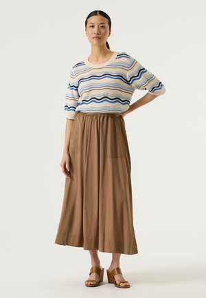 Pull en maille avec un motif ondulé bleu et crème, associé à une jupe midi marron avec une taille élastique et des poches. Sandales marron à talons blocs.