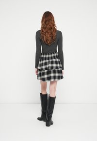 Black and white plaid flared skirt with smocked waist, paired with a fitted gray top and knee-high black leather boots.