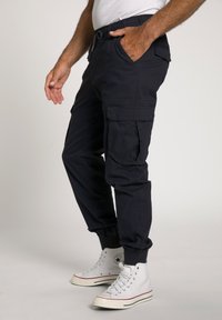 Navy cargobroek met elastische tailleband, zijzakken en taps toelopende boorden, gedragen met witte hoge sneakers. Gladde stoftextuur.