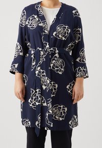 Mörkblå omlottkappa med vita rosor, långa ärmar och ett knytbälte i midjan, tillverkad av ett lätt tyg.