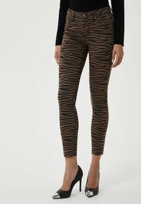 Jeans ajustados de estampado de cebra marrón con acentos negros, que presentan una cintura alta, bolsillos frontales y un dobladillo deshilachado, combinados con tacones negros de punta.
