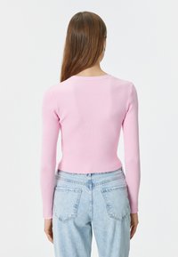 Top a maniche lunghe a coste di colore rosa chiaro con scollatura tonda, abbinato a jeans a vita alta azzurri chiari con tasche posteriori e vestibilità casual.