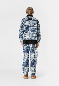 Conjunto de chaqueta y pantalones azul y blanco con un diseño estampado, que presenta un corte relajado, tejido texturizado, cuello negro y detalle de etiqueta lateral.