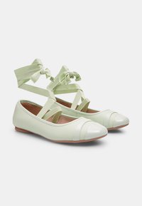 Gaiši zaļi baleta kurpītes ar spīdīgu purngalu, elastīgām krusteniskajām siksnām un gludu ādas līdzīgu tekstūru. Apdarinātas ar horizontālām rieviņām.