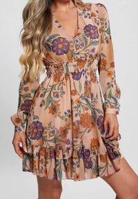 Vestido floral en melocotón con flores moradas y naranjas, de manga larga y con cintura fruncida. Presenta un dobladillo con volantes y un diseño de escote en V.