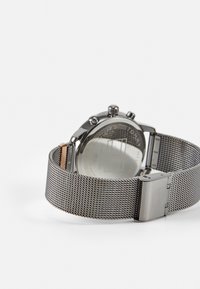 Reloj de acero inoxidable con pulsera de malla, que presenta una caja de acero inoxidable texturizada y un fondo de cristal. El cierre tiene un acabado plateado y elegante.
