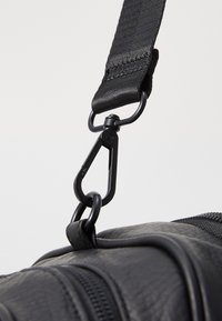 Bandoulière de sac noir en tissu texturé, avec un clip de libération rapide noir mat et des coutures renforcées près de la quincaillerie.