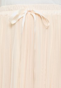 Gonna in tulle leggera e plissettata di un delicato colore pesco, con un nastro in satin liscio in corrispondenza della vita per una vestibilità sicura.