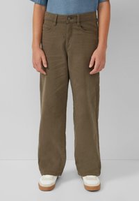 Olijfgroene wijde broek met een gladde stofafwerking, vijf zakken en een knoopsluiting, gecombineerd met witte sneakers.