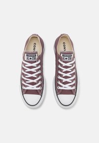 Burgundijske platnene tenisice s bijelim vezicama i gumenim đonovima, s crno-bijelim "Converse All Star" logotipom na jeziku.