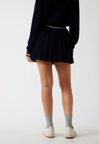 Marineblaue Faltenrock mit einem schmalen Taillenbund, kombiniert mit grauen Rippensocken und weißen Sneakers. Weicher Stoff, klare Linien und mehrschichtiges Design.