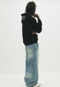 Sort oversized hoodie med logo på ryggen, parret med lyseblå vidde denim jeans med slidte detaljer og en afslappet pasform.