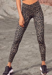 Leggings a stampa leopardata realizzati in tessuto elasticizzato, con un alto punto vita e un design aderente, abbinati a scarpe da ginnastica nere.