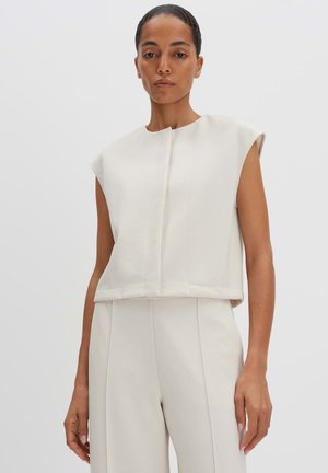 Gekürzte, ärmellose cremefarbene Bluse mit rundem Ausschnitt und subtilen Stickdetails. Glatte Textur, kombiniert mit passenden Hosen.