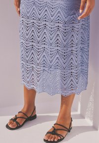 Jupe en dentelle bleu clair avec un motif en zigzag et des découpes, associée à des sandales à brides noires tressées. Texture lisse et design en couches.