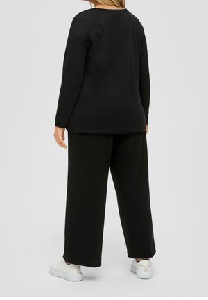 Haut noir à manches longues associé à un pantalon noir à jambes larges, le tout en tissu doux. La tenue est complétée par des baskets blanches.