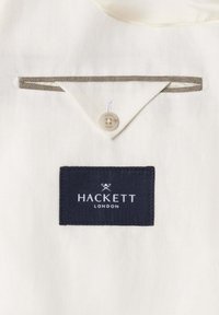 Hvidt tøjindvendigt med trekantet knappet klap og lomme med grå kant over navy Hackett London mærkeetiket.