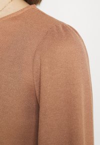 Pull en maille côtelée marron présentant un tissu texturé, une forme ajustée et des manches légèrement bouffantes, mettant en avant son design contemporain.