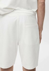 Shorts en tricot blancs avec une texture lisse, une taille élastique et une poche arrière unique avec un détail de couture subtil.