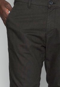 Pantaloni grigio scuro con finitura testurizzata, dotati di chiusura con bottone e zip, tasche laterali e taglio standard.