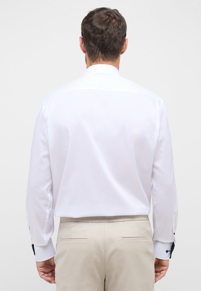 Witte lange mouwen shirt met een standaard kraag, gladde textuur en contrasterende marineblauwe accenten op de manchet, gecombineerd met beige broek.