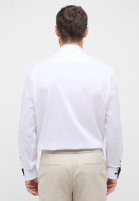 Biała koszula na guziki z długimi rękawami, z kontrastującymi granatowymi akcentami na mankietach oraz gładką, lekką fakturą materiału.