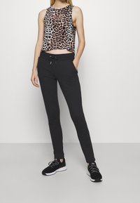 Cropped tanktop met luipaardprint en zwarte joggers met elastische tailleband en trekkoord; gecombineerd met zwarte sportschoenen.