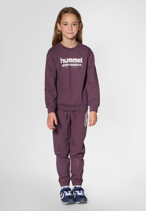 Lilla bomuldssweatshirt med "hummel"-logo, kombineret med matchende joggers med logoaccenter. Mørke sportssko fuldender outfittet.