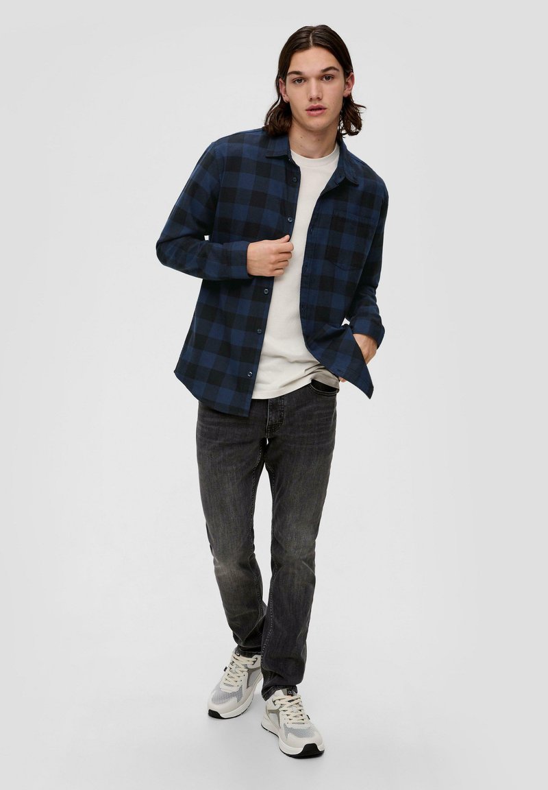 Marineblauw en zwart geruit flanellen shirt met knoopsluiting, gedragen over een witte t-shirt, gecombineerd met donkere spijkerbroek en sportschoenen.