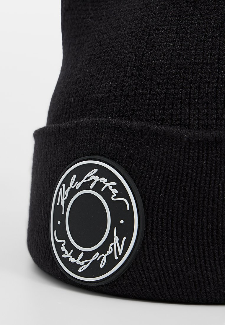 Czarna dzianinowa czapka beanie z szerokim mankietem i okrągłą gumową naszywką z białym podpisem. Miękka faktura z prążkowanym wzorem.