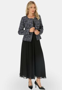 Granatowa i biała marynarka z tweedu, z okrągłym dekoltem i złotym guzikiem, w połączeniu z długą czarną sukienką i czarnymi szpilkami.