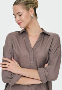 Brun, knappet op, langærmet skjorte med en afslappet pasform. Blød tekstur og en krave, med oprullede ærmer og to synlige knapper.