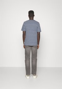 Páskované námořnické modré a bílé bavlněné tričko s krátkým rukávem, spárované se šedými džíny a bílými teniskami s logem značky na zadní straně.