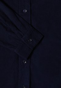 Camicia di velluto a coste blu navy con maniche lunghe, chiusura a bottoni sul davanti e tessuto testurizzato con righe verticali. Bottoni neri lungo la listarella.
