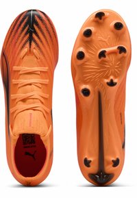 Scarpe da calcio arancioni luminose con una tomaia testurizzata, dettagli neri e una suola a motivi con sei tacchetti neri per la trazione.