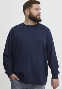 Felpa blu navy realizzata in tessuto morbido con collo giro, maniche lunghe e polsini a coste, caratterizzata da un piccolo badge con logo vicino all'orlo.