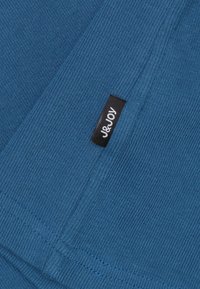 Blauwe gebreide stof met een soepele textuur; heeft een zwart etiket met "J&Joy" in het wit gedrukt, gepositioneerd op de onderste rand.