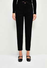 Jeans negros de cintura alta con ajuste tapered, tela de denim texturizada, bolsillos frontales y cierre de botón dorado. Se incluye un par de ballerinas negras.