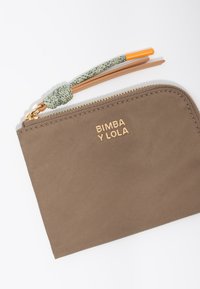 Brązowy portfel z tkaniny z złotym logo "BIMBA Y LOLA", o teksturowanej powierzchni i plecionym uchwycie suwaka w kolorze zielonym i pomarańczowym. Prostokątny kształt.