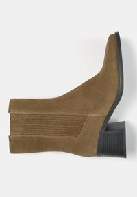Bottine en suede marron avec un bout pointu, des détails de couture verticale et un talon bloc noir texturé. Texture lisse et design élégant.
