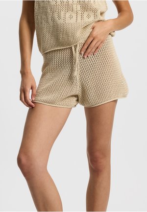 Beige strikket crop top med åben vævning og logodetalje, kombineret med matchende strikkede shorts med elastisk snørebånd i taljen.