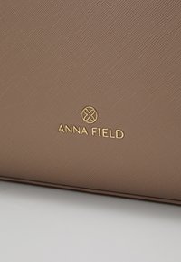 Brown textured synthetic leather with a gold logo that reads "ANNA FIELD" centered below a circular emblem.