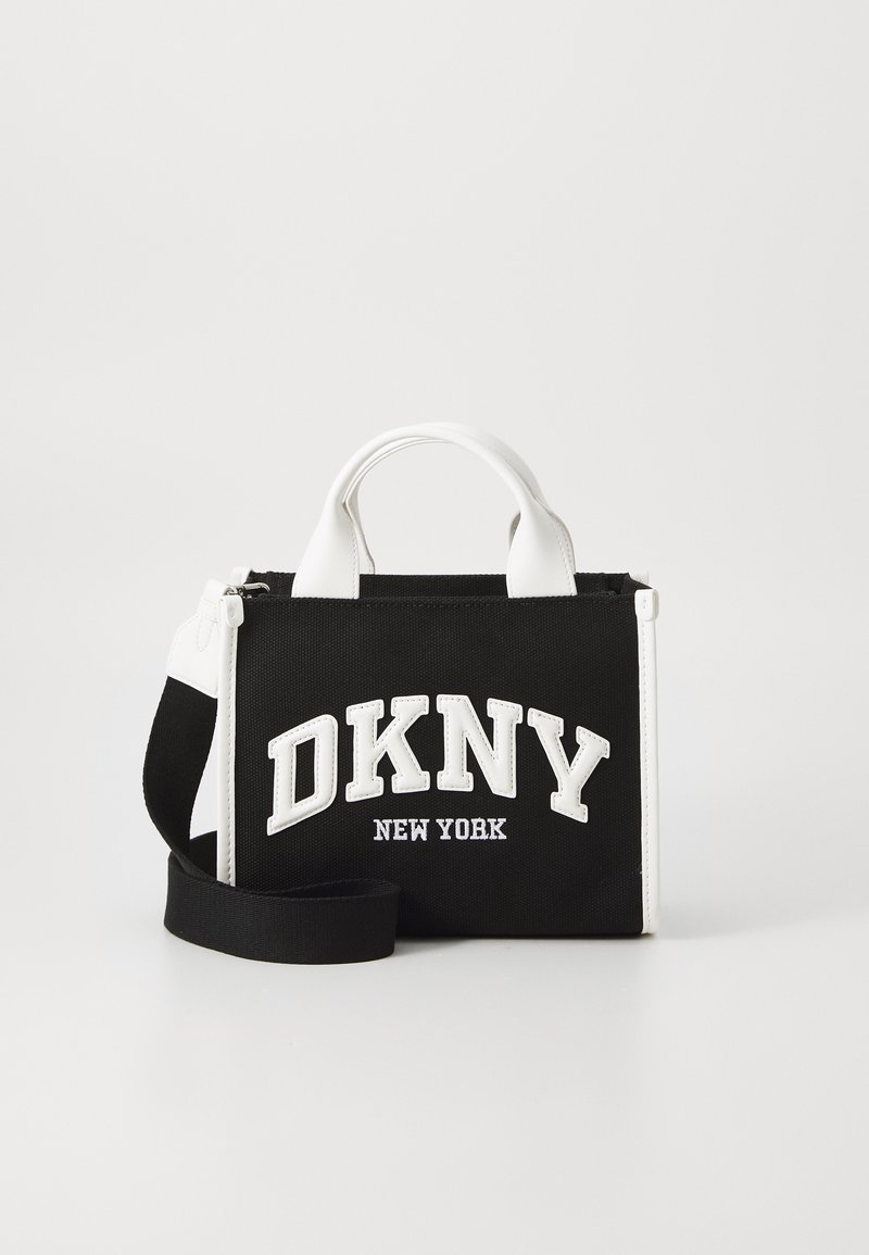 Sac à main noir en toile avec des accents en cuir blanc. L'avant présente le logo en lettres surélevées blanches "DKNY NEW YORK". Comprend des poignées courtes et une bandoulière amovible.